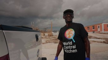 Movie still from “We Feed People” (2022), directed by Ron Howard – A man standing in front of a car on a road; Medium shot, Low angle
