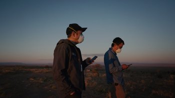Movie still from “We Feed People” (2022), directed by Ron Howard – Two men wearing face masks while looking at their cell phones; Medium shot, Low angle