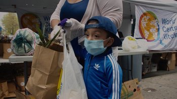 Movie still from “We Feed People” (2022), directed by Ron Howard – A woman and a child wearing masks and gloves; Medium shot, Low angle