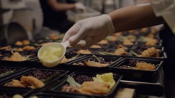 Movie still from “We Feed People” (2022), directed by Ron Howard – A person in a white glove putting a spoon into a container of food; Extreme Close Up shot, High angle