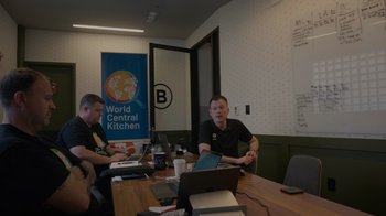 Movie still from “We Feed People” (2022), directed by Ron Howard – A group of people sitting at a table with laptops; Wide shot, Over the shoulder angle