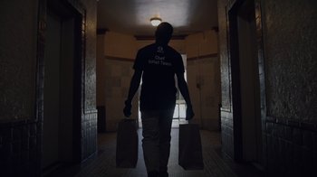 Movie still from “We Feed People” (2022), directed by Ron Howard – A man walking down a hallway with two bags of food; Medium shot, Low angle