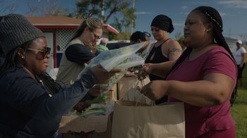 Movie still from “We Feed People” (2022), directed by Ron Howard – A group of people standing next to each other holding bags; Medium shot, Low angle