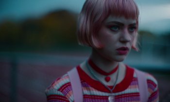 A girl with pink hair is standing outside