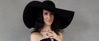 Movie still from “WeWork: Or the Making and Breaking of a $47 Billion Unicorn” (2021), directed by Jed Rothstein – A woman wearing a large black hat and posing for a picture; Close Up shot, Low angle