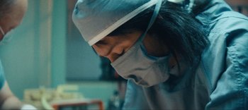 Movie still from “Weird: The Al Yankovic Story” (2022), directed by Eric Appel – A woman wearing a surgical mask and a surgical cap; Extreme Close Up shot, Low angle