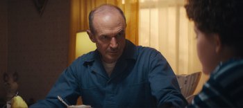 Movie still from “Weird: The Al Yankovic Story” (2022), directed by Eric Appel – An older man sitting at a table in front of a window; Medium shot, Low angle