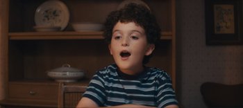 Movie still from “Weird: The Al Yankovic Story” (2022), directed by Eric Appel – A young boy with curly hair is sitting in a chair; Close Up shot, High angle