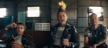 Movie still from “Weird: The Al Yankovic Story” (2022), directed by Eric Appel – A man with a mohawk is sitting on a bench; Medium shot, Low angle