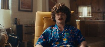 Movie still from “Weird: The Al Yankovic Story” (2022), directed by Eric Appel – A man sitting in a chair wearing a hawaiian shirt; Medium shot, Over the shoulder angle