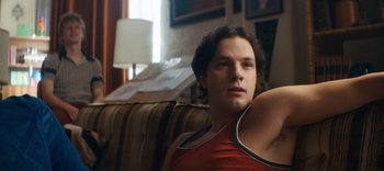 Movie still from “Weird: The Al Yankovic Story” (2022), directed by Eric Appel – A man sitting on top of a couch in a living room; Close Up shot, Low angle