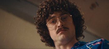 Movie still from “Weird: The Al Yankovic Story” (2022), directed by Eric Appel – A man with a mustache and curly brown hair wearing glasses; Close Up shot, Low angle