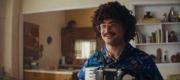 Movie still from “Weird: The Al Yankovic Story” (2022), directed by Eric Appel – A man with a curly hair and glasses is holding a camera; Medium shot, Over the shoulder angle