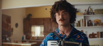 Movie still from “Weird: The Al Yankovic Story” (2022), directed by Eric Appel – A man in a blue shirt is playing an accordian; Close Up shot, Over the shoulder angle