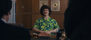 Movie still from “Weird: The Al Yankovic Story” (2022), directed by Eric Appel – A man in a hawaiian shirt sitting at a table; Medium shot, Over the shoulder angle