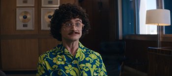 Movie still from “Weird: The Al Yankovic Story” (2022), directed by Eric Appel – A man with a mustache and curly brown hair wearing glasses; Close Up shot, Over the shoulder angle