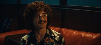 Movie still from “Weird: The Al Yankovic Story” (2022), directed by Eric Appel – A man sitting on top of an orange couch; Close Up shot, Over the shoulder angle