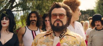 Movie still from “Weird: The Al Yankovic Story” (2022), directed by Eric Appel – A man with a beard wearing a tie and sunglasses; Medium shot, Low angle