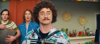 Movie still from “Weird: The Al Yankovic Story” (2022), directed by Eric Appel – A man with a mustache and curly hair holding a rifle; Medium shot, Over the shoulder angle