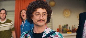 Movie still from “Weird: The Al Yankovic Story” (2022), directed by Eric Appel – A man with curly brown hair wearing glasses and a hawaiian shirt; Close Up shot, Over the shoulder angle
