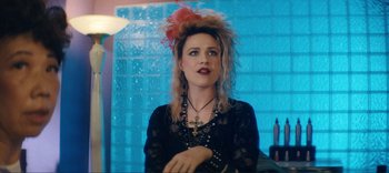 Movie still from “Weird: The Al Yankovic Story” (2022), directed by Eric Appel – A woman in a black dress with a pink feather in her hair; Close Up shot, Over the shoulder angle