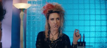 Movie still from “Weird: The Al Yankovic Story” (2022), directed by Eric Appel – A woman with a red feather mohawk and a cross necklace; Close Up shot, Overhead angle