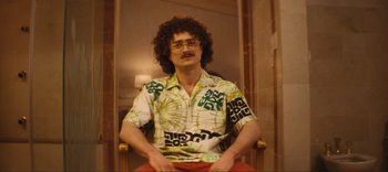 Movie still from “Weird: The Al Yankovic Story” (2022), directed by Eric Appel – A man sitting in a chair wearing a hawaiian shirt; Medium shot, High angle