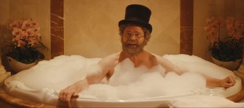 Movie still from “Weird: The Al Yankovic Story” (2022), directed by Eric Appel – A bearded man wearing a top hat in a bath tub; Medium shot, Over the shoulder angle