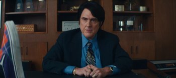 Movie still from “Weird: The Al Yankovic Story” (2022), directed by Eric Appel – A man sitting at a desk in a suit and tie; Medium shot, Low angle