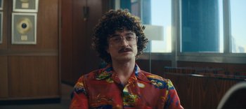 Movie still from “Weird: The Al Yankovic Story” (2022), directed by Eric Appel – A man in a red shirt and glasses is staring straight ahead; Medium shot, Over the shoulder angle