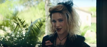 Movie still from “Weird: The Al Yankovic Story” (2022), directed by Eric Appel – A woman with a black bow in her hair holding a stick in her mouth; Close Up shot, Over the shoulder angle