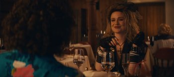 Movie still from “Weird: The Al Yankovic Story” (2022), directed by Eric Appel – A woman sitting at a table with a glass of red wine; Medium shot, Over the shoulder angle