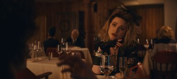 Movie still from “Weird: The Al Yankovic Story” (2022), directed by Eric Appel – A woman sitting at a table with a glass of wine; Medium shot, Over the shoulder angle
