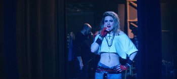 Movie still from “Weird: The Al Yankovic Story” (2022), directed by Eric Appel – A woman in a white shirt and a cross on her chest; Medium shot, Over the shoulder angle