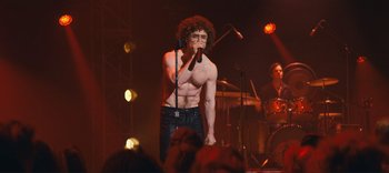 Movie still from “Weird: The Al Yankovic Story” (2022), directed by Eric Appel – A shirtless man singing into a microphone on a stage; Wide shot, Over the shoulder angle