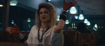 Movie still from “Weird: The Al Yankovic Story” (2022), directed by Eric Appel – A person with long blonde hair wearing a white shirt and red gloves; Medium shot, Low angle