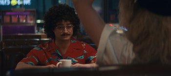 Movie still from “Weird: The Al Yankovic Story” (2022), directed by Eric Appel – A man in a hawaiian shirt and glasses holding a coffee mug; Medium shot, Over the shoulder angle