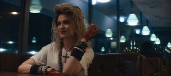 Movie still from “Weird: The Al Yankovic Story” (2022), directed by Eric Appel – A woman with long blonde hair wearing a white shirt and bracelets; Close Up shot, Over the shoulder angle