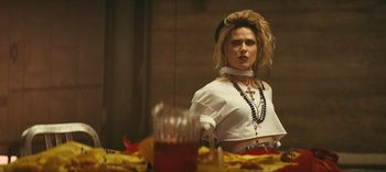 Movie still from “Weird: The Al Yankovic Story” (2022), directed by Eric Appel – A woman standing in front of a table with food on top of it; Medium shot, Low angle