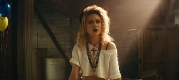 Movie still from “Weird: The Al Yankovic Story” (2022), directed by Eric Appel – A woman wearing a white shirt and a cross necklace; Medium shot, Over the shoulder angle