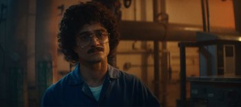 Movie still from “Weird: The Al Yankovic Story” (2022), directed by Eric Appel – A man with a beard and glasses is standing in a room; Close Up shot, Over the shoulder angle