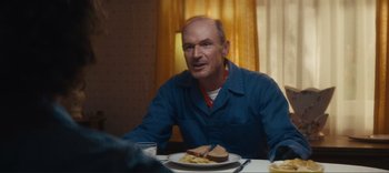 Movie still from “Weird: The Al Yankovic Story” (2022), directed by Eric Appel – A man sitting at a table with a plate of food; Medium shot, Over the shoulder angle