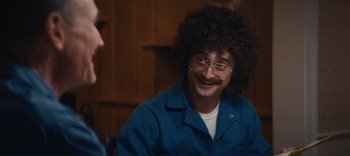 Movie still from “Weird: The Al Yankovic Story” (2022), directed by Eric Appel – A man in a blue shirt with a fake mustache and curly hair; Close Up shot, Over the shoulder angle