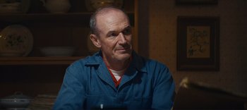 Movie still from “Weird: The Al Yankovic Story” (2022), directed by Eric Appel – An older man wearing a blue shirt is sitting at a table; Close Up shot, Low angle