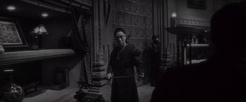 Movie still from “Werewolf by Night” (2022), directed by Michael Giacchino – A man in a black robe holding a sword in front of a wall; Medium shot, High angle