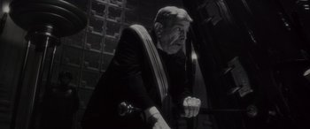 Movie still from “Werewolf by Night” (2022), directed by Michael Giacchino – An older man in a suit and tie looking at the camera; Medium shot, Low angle