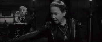 Movie still from “Werewolf by Night” (2022), directed by Michael Giacchino – An older woman wearing a leather jacket and a cross necklace; Close Up shot, Over the shoulder angle