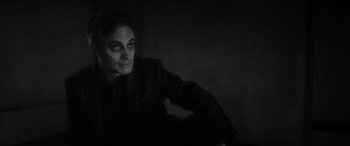 Movie still from “Werewolf by Night” (2022), directed by Michael Giacchino – A man in a black suit sitting in front of a wall; Close Up shot, Low angle