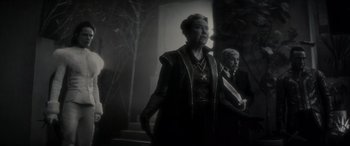 Movie still from “Werewolf by Night” (2022), directed by Michael Giacchino – An older woman standing next to an older man; Medium shot, Over the shoulder angle