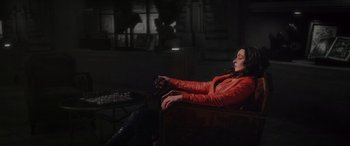 Movie still from “Werewolf by Night” (2022), directed by Michael Giacchino – A woman sitting in a chair holding a remote control; Medium shot, High angle